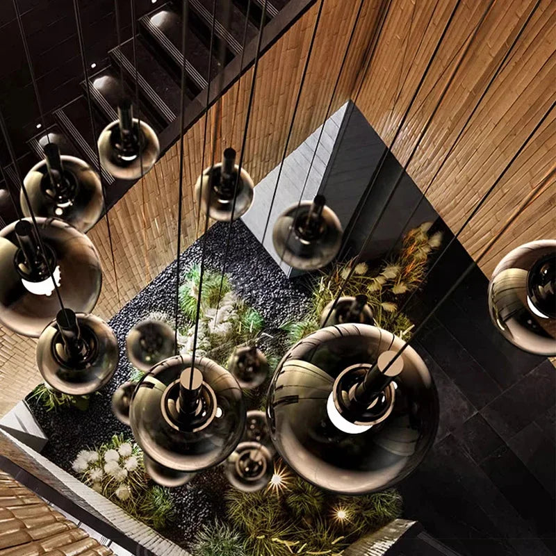Nordic Stair Chandelier — Living & Dining Room Pendant Ceiling Light featuring multiple modern glass pendants suspended over an indoor garden with warm wood and dark stone accents in a minimalist space.