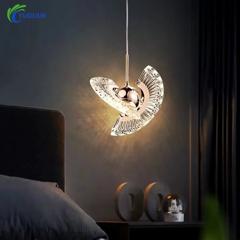 Rose gold pendant light with curved crystal wings glowing above a bedside table