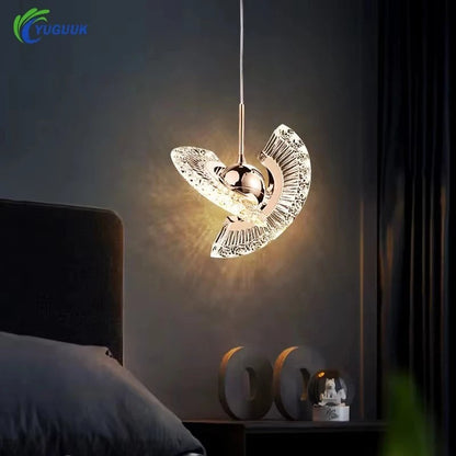 Rose gold pendant light with curved crystal wings glowing above a bedside table