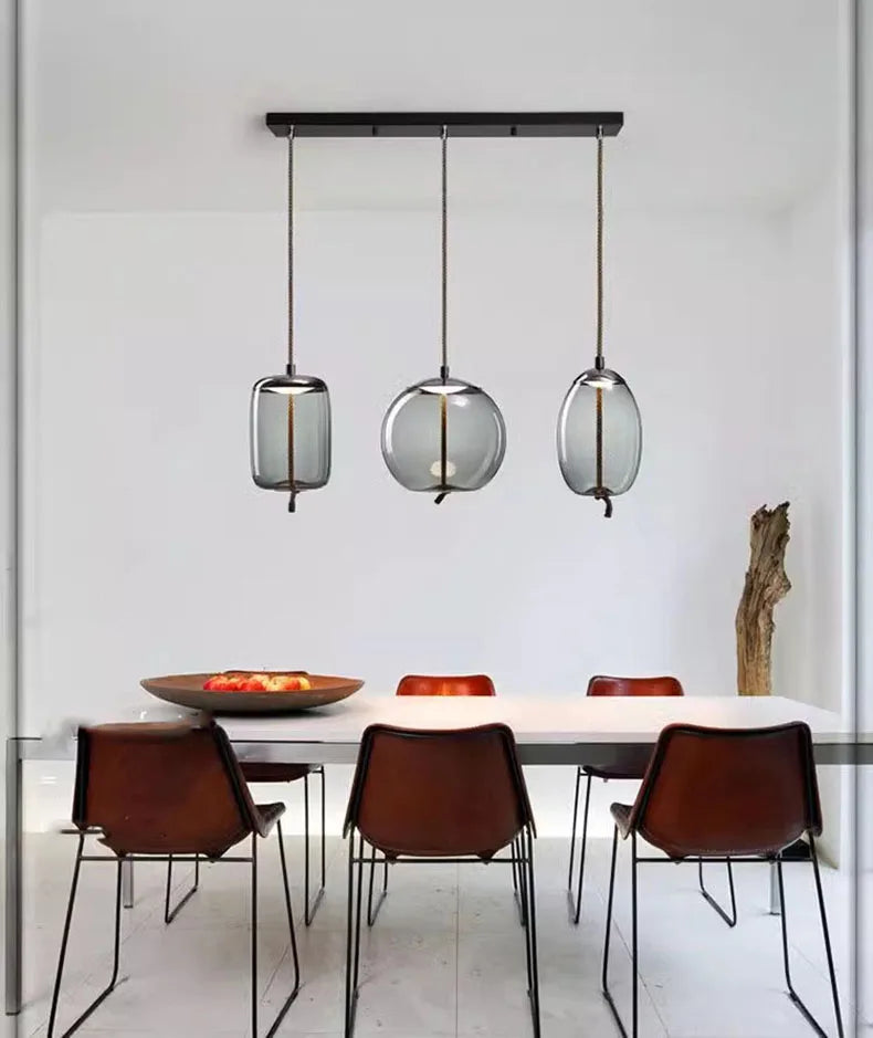 Minimalist dining room featuring a Modern LED Pendant Light — Chandelier for Living & Dining Room with three smoked glass globes above a white table and brown leather chairs.
