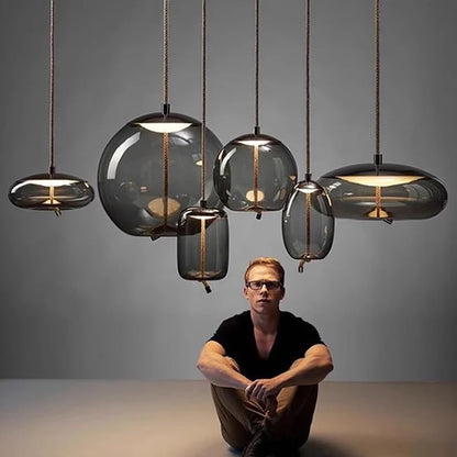 A man sitting cross-legged under a group of suspended glass shapes with warm light glowing inside, showcasing the Modern LED Pendant Light — Chandelier for Living & Dining Room in a minimalist setting.