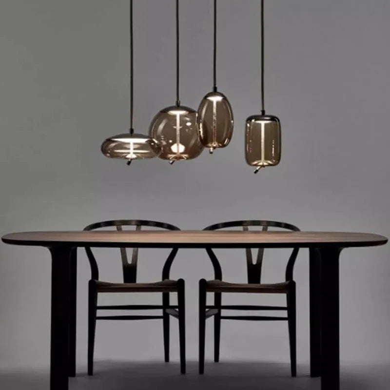 Modern LED Pendant Light — Chandelier for Living & Dining Room featuring four elegant glass shades hanging above a minimalist wooden dining table with two black chairs, ideal for luxury home décor.