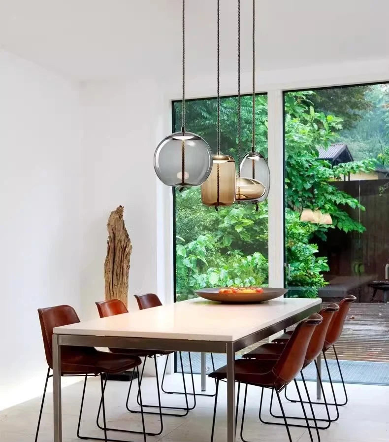 Modern LED Pendant Light — Chandelier for Living & Dining Room hanging above a minimalist dining table with brown leather chairs, featuring a large window with a lush green outdoor view.