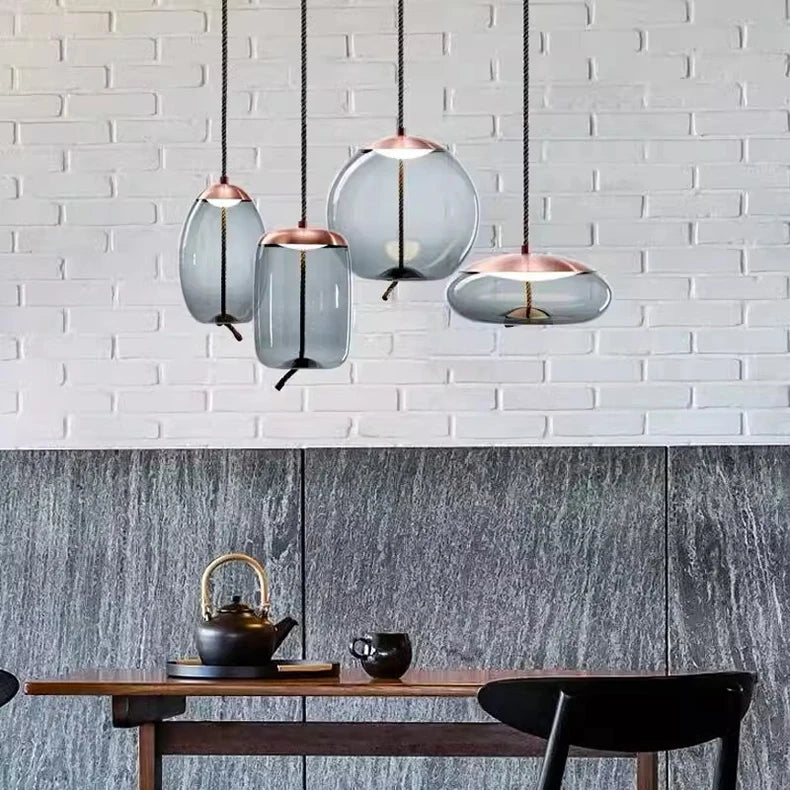 Modern LED Pendant Light — Chandelier for Living & Dining Room with four delicate glass shades in varied shapes hanging over a minimalist wooden table set against a textured wall.