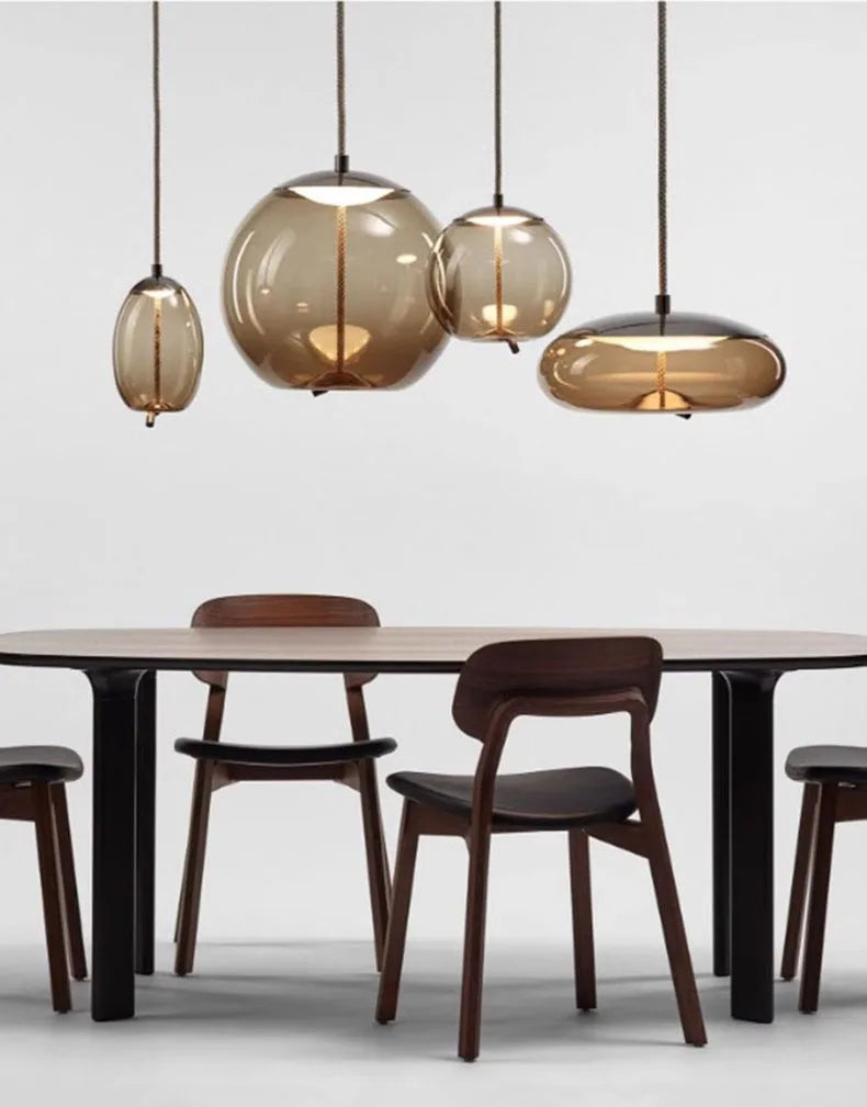 Modern LED Pendant Light — Chandelier for Living & Dining Room featuring four warm-toned glass pendant lights suspended over a minimalist wooden dining table with dark chairs, blending Nordic design and luxury home décor.