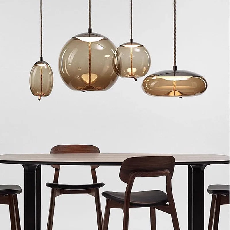 Minimalist dining area featuring a Modern LED Pendant Light — Chandelier for Living & Dining Room with amber glass shades hanging over a sleek wooden table and dark chairs.